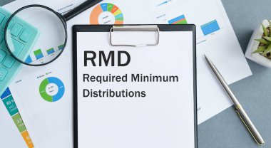 Masada raporlar, bir büyüteç, bir hesap makinesi, bir kalem ve içinde RMD gerektiren Minimum Dağıtımlar olan beyaz bir defter var.