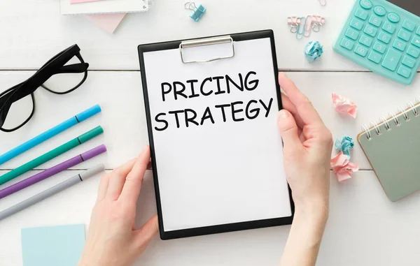 Masada raporlar, bir büyüteç, bir hesap makinesi, bir kalem ve üzerinde STRATEGY yazan beyaz bir defter var. İş konsepti
