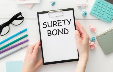 SURETY BOND text on notepad with laptop on the white wooden background clipart