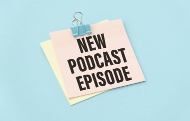 Kırsal ahşap masadaki podcast kayıt ekipmanlarının en üst görüntüsü. Spiral not defterinde yeni podcast bölümü yazıyor.