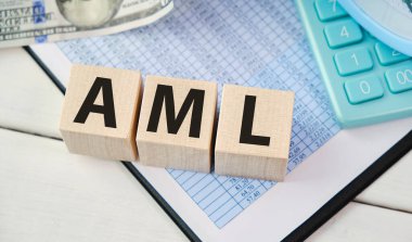 Masadaki tahta küplere not defteri ve hesap makinesiyle yazılmış AML kelime kavramı