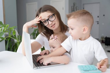 Evde dizüstü bilgisayarla çalışan kendini işine adamış genç kadınların dikkatini dağıtan küçük çocuklar. Evden çalışma kavramı.