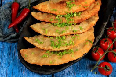 Sıcak ev yapımı chebureki turtaları kıyma, tabakta soğan ve biber, ahşap arka plan.