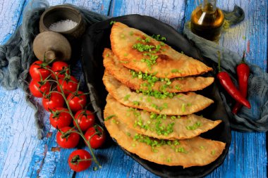 Sıcak ev yapımı chebureki turtaları kıyma, tabakta soğan ve biber, ahşap arka plan.