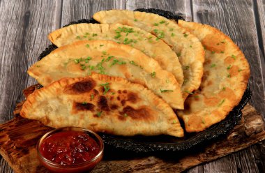Sıcak ev yapımı chebureki turtaları kıyma, tabakta soğan ve biber, ahşap arka plan.
