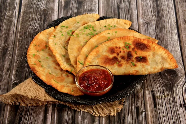 Sıcak ev yapımı chebureki turtaları kıyma, tabakta soğan ve biber, ahşap arka plan.