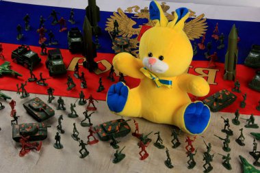 Ukrayna 'nın ulusal renklerdeki oyuncak tavşanı Rus ve Amerikan bayraklarının arka planında teneke askerler ve zırhlarla çevrilidir. Rusya ve ABD Ukrayna 'da. Askerlerin ve topçuların rakamları