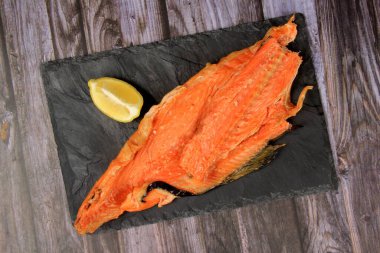 Sıcak füme somon, alabalık kemikleri ve siyah taş tabakta limon. Koyu tahta arkaplan.