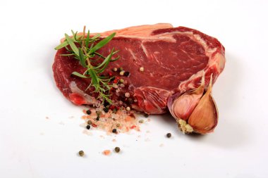 Raw sirloin beef steak with rosemary, pepper, salt and garlic on white background