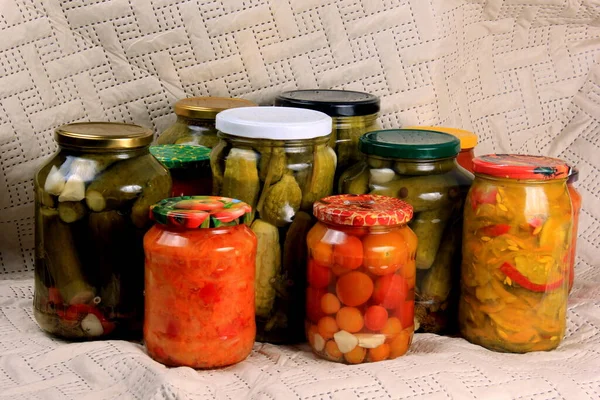 Glass jars with pickles and canned vegetables on a blanket. Canned cucumbers
