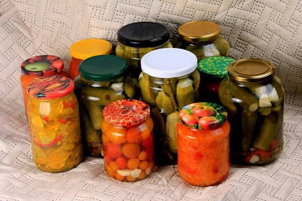 Glass jars with pickles and canned vegetables on a blanket. Canned cucumbers