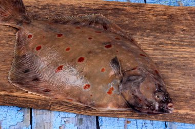 Soğan, sarımsak ve baharatla süslenmiş ahşap bir tahta üzerinde taze deniz balığı plazası (Pleuronectes platessa). Mavi ahşap arka plan