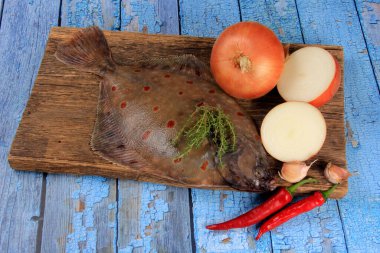 Soğan, sarımsak ve baharatla süslenmiş ahşap bir tahta üzerinde taze deniz balığı plazası (Pleuronectes platessa). Mavi ahşap arka plan
