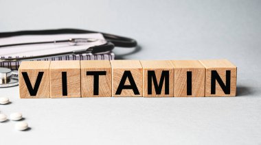 Beyaz arka planda izole edilmiş tahta küplere yazılmış VITAMIN yazıtları, tıp konsepti. Masanın yanında steteskop ve haplar var..