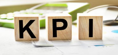 Tahta küplerin dokusunda KPI yazıları var. Hesap makinesi ve iş belgelerinin arka planında tahta küpler var. Finansal, ticari ya da ekonomik tema üzerine bir yazı.