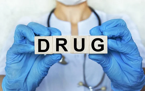 医師の女性の保護手袋で手の中の木製の立方体ブロック上の単語の薬物 背景に医師を刺激します — ストック写真