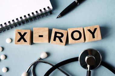 Wooden cubes with the inscription X ROY lie on the table. View from above. Nearby is a stethoscope, a notebook and scattered pills.