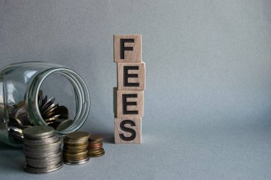 Tahta küplerdeki yazıt ücretleri hafif bir zemin üzerinde izole edilmiş. Yanında madeni paralar, iş ve finans kavramlarıyla dolu cam bir kavanoz..