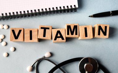 Üzerinde VITAMIN yazan tahta küpler masanın üzerinde duruyor. Yukarıdan bak. Yakınlarda steteskop, defter ve dağınık haplar var..