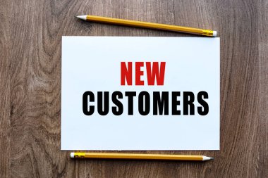NEW CUSTOMERS metni ahşap bir masanın üzerinde duran bir deftere yazılmıştır. İş ya da finans temalı bir mektup. İş konsepti.