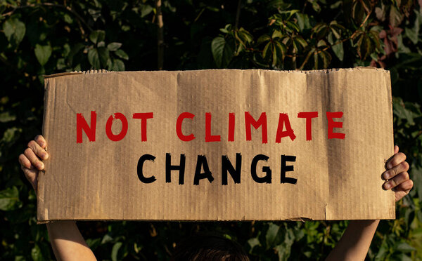 A poster with the words NOT CLIMATE CHANGE in the hands of a young girl on a background of green foliage.