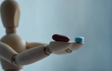 Elinde iki hap tutan tahta bir adam figürü. Arka planda, mesajın için boş bir alan var. Tıp ve sağlık hizmetleri kavramı.
