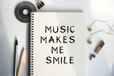 Defterdeki yazı müzik beni gülümsetiyor. Kahve, kulaklık ve defterleri olan sessiz bir iş yeri. Rahatlatıcı müzikle bir anlık rahatlama ve kopukluk. Yukarıdan görüntüle.