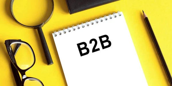 B2B 'den işe, sarı arka planda, gözlüklü, büyüteçli ve kalemli bir not defteri. İş konsepti.