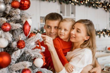 Mutlu anne, küçük oğluna kırmızı Noel balosunu ve evdeki Noel ağacının yanında gülen kocasını gösteriyor.