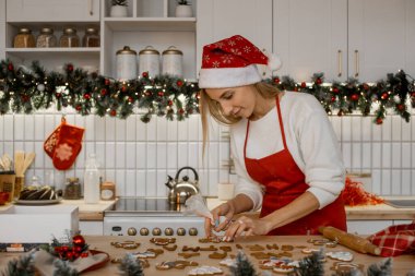 Noel pastanesini dekore ediyorum. Noel Baba şapkalı kadın mutfak masasında ev yapımı zencefilli kurabiye pişiriyor.