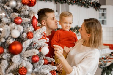 Genç ebeveynler oynaşıp oğluyla oynuyorlar. Mutlu aile Noel ağacının yanında eğleniyor.