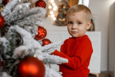 Gülümseyen küçük çocuk evde Noel ağacını süslüyor.