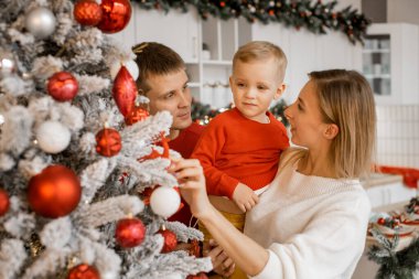 Mutlu genç aile Noel ağacını süsleyerek tatillerinin tadını çıkarıyor.