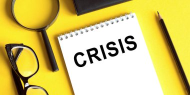 Sarı arkaplanda CRISIS yazılı bir not, gözlük, büyüteç ve bir kalem.