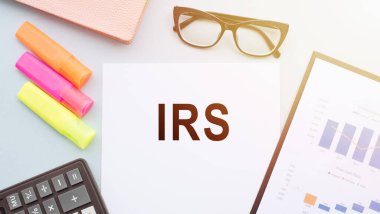 IRS International Revenue Service text on notebook with glasses, calculator and color markers on white background