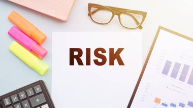 Hesap makinesi, kalem, gözlük ve mali tablolarla ofis masasındaki RISK metni.