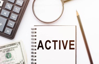 Masasında hesap makinesi, dolar ve büyüteçle AcTIVE notu olan not defteri..
