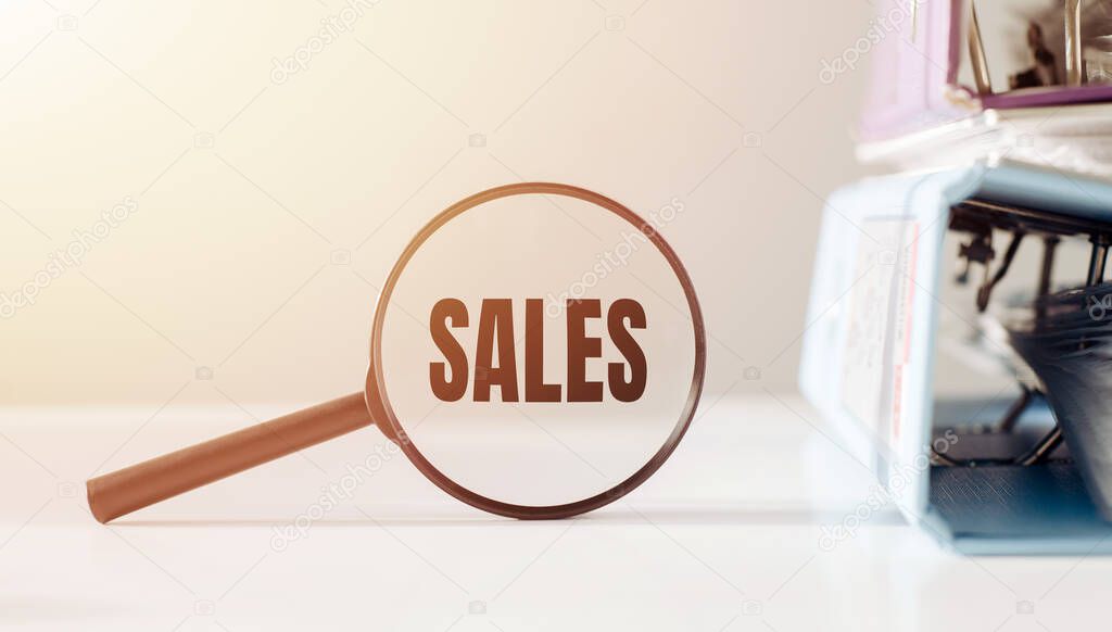 Magnifying glass with the word SALES on office table.