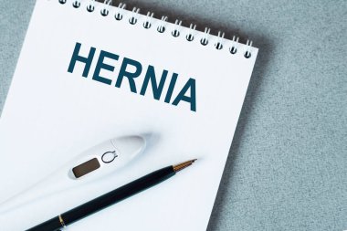 Masanın üzerinde termometre ve kalem olan boş bir defter. HERNIA metni.