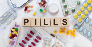 Masanın üzerindeki tahta bloklarda PILLS sözcüğü. Arka planda haplar, vitaminler, steteskop ve şırınga ile tıbbi konsept.