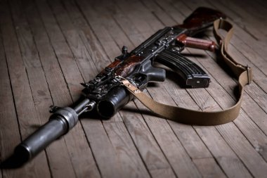 Tahta arka planda susturucusu olan izole edilmiş Kalaşnikof saldırı tüfeğini kapatın.