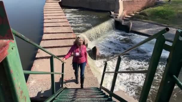 阳光灿烂的一天 戴着太阳镜的快乐的成年女子走上楼梯 走向大坝大门 布宜诺斯艾利斯San Antonio Areco — 图库视频影像