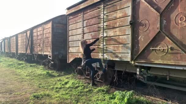 一个成年妇女爬上一辆废弃的火车货车的侧梯 被遗弃地点概念 — 图库视频影像