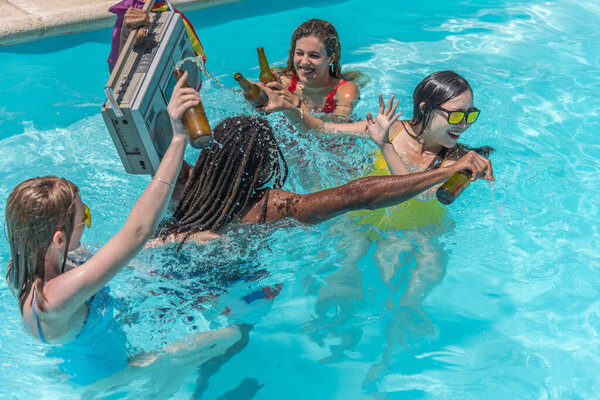 People playing splash around inside a pool with beers while a man carries a cassette player with a rainbow flag