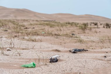 Plastik şişeler kumsalın yakınındaki kumların üzerinde, arka planda kum tepeleri vardı. Dünyaya göz kulak ol..