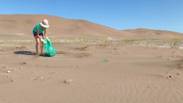 Volwassen vrouw met een witte hoed en groene handschoenen die vuilnis in een groene tas verzamelt. Conceptverstopping — Stockvideo