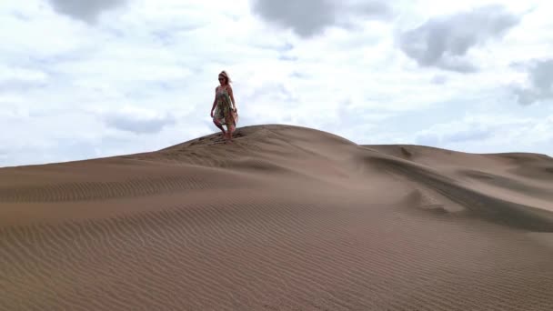 View from below a big dune of a woman descending with mobile phone in hand. — Video