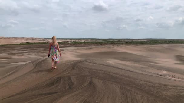 View from behind of a blonde woman in a colorful beach dress walking along the top of a big medano — Stockvideo