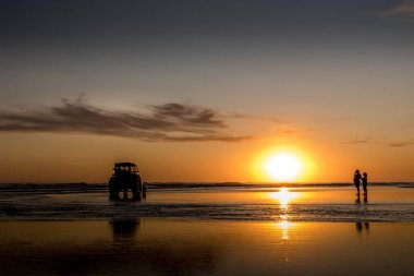Traktör ve bir çift gün batımında sahilde denizin üzerinde..