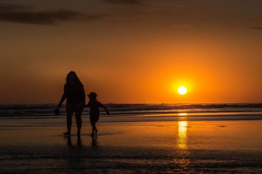 Gün batımında sahilde yürüyen anne ve çocuğun sudaki yansıması..